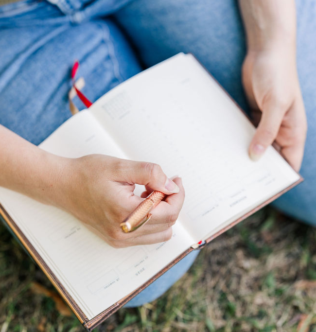 Elena, a translator and copywriter in Nürnberg light blue jeans sitting with legs on the side and a notebook on her lap, writing. Picture taken from above.